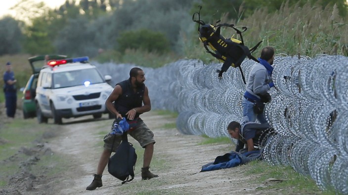 Hungarian police positioned nearby watch as Syrian migrants climb under a fence to enter Hungary at the Hungarian-Serbian border near Roszke
