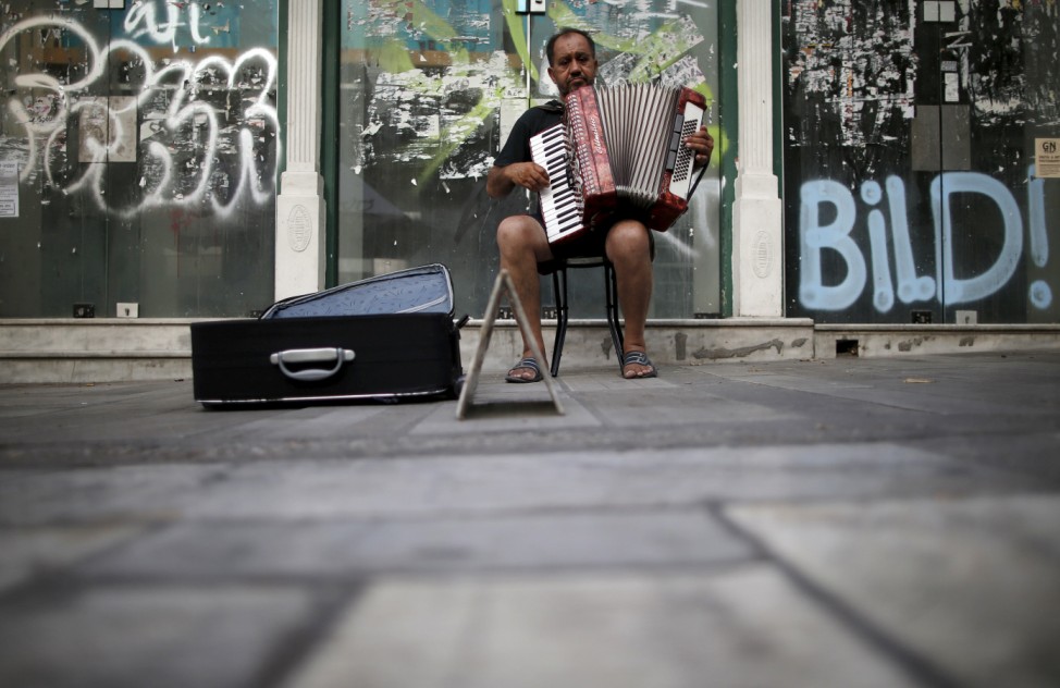 A street musician plays the accordion in front of a closed store in central Athens