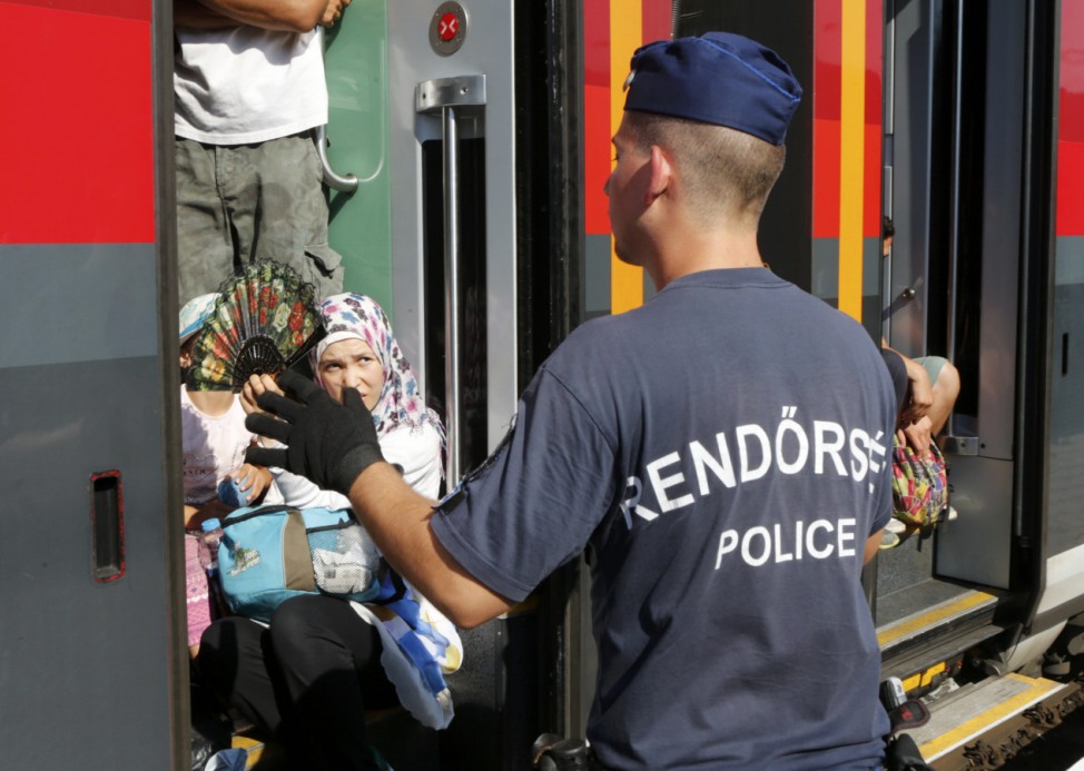 A Hungarian police officer gestures to travellers as a train heading for Austria, with migrants on board, is stopped for checks at a border station in Hegyeshalom
