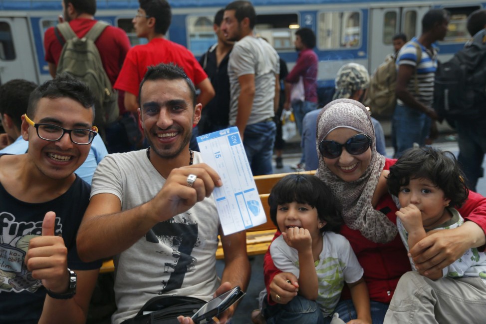 Migrants pose with a train ticket as they wait for a train to Austria at a train station in Budapest