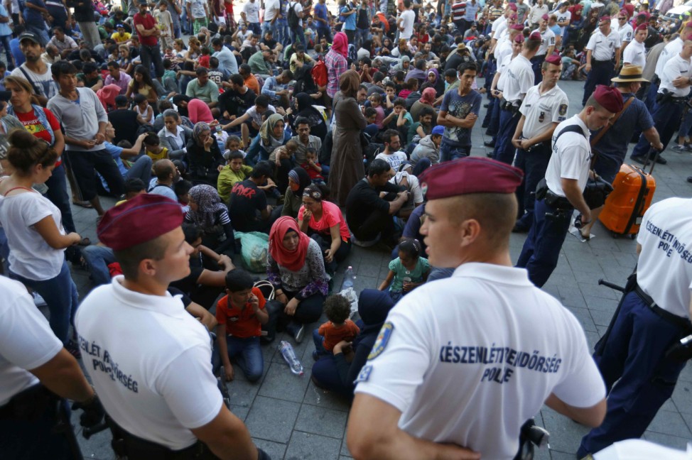 Hungarian police officers watch migrants outside the main Eastern Railway station in Budapest