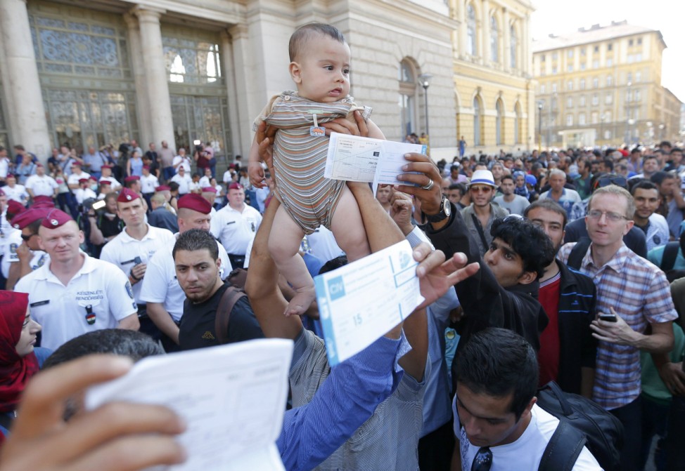 Migrants wave their train tickets and lift up children outside the main Eastern Railway station in Budapest