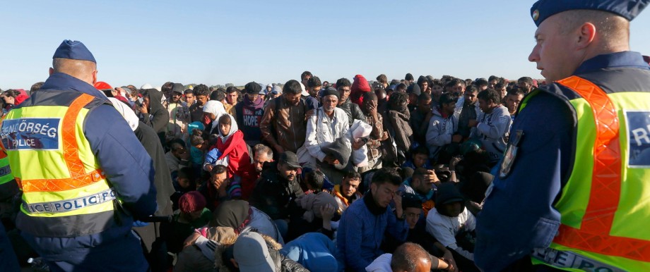 Migrants wait for buses behind police at collection point in Roszke