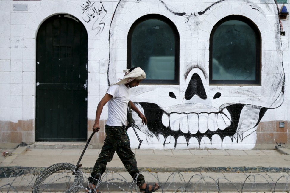 Houthi militant walks past graffiti painted by pro-Houthi activists on gate of Saudi embassy in Yemen's capital Sanaa