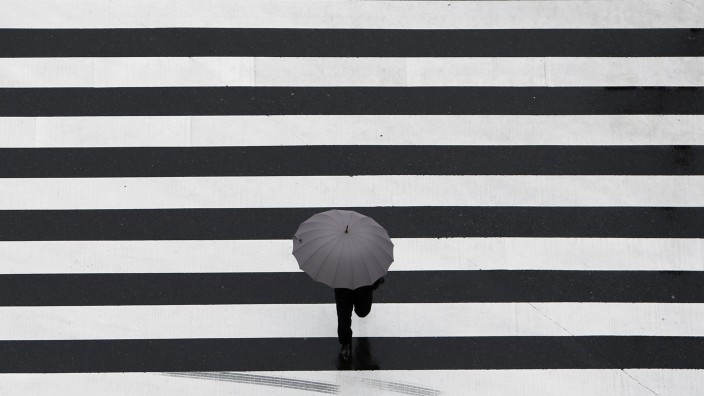 Man holding an umbrella crosses a street at a business district in Tokyo