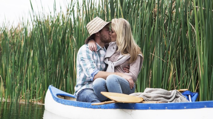 Young couple kissing in a canoe on a lake hiding behind straw hat model released Symbolfoto property