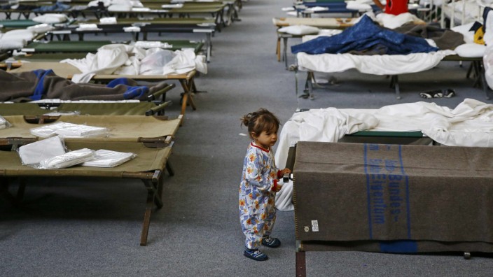 A migrant child stands next to a bed at an improvised temporary shelter in a sports hall in Hanau