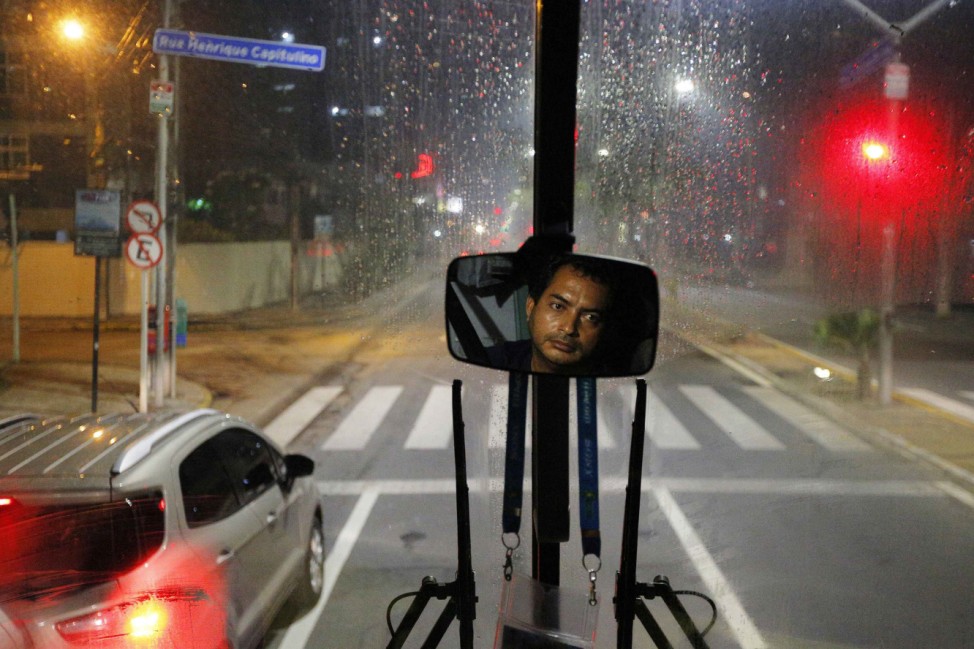 The media bus driver is reflected in a mirror during the trip away from the Pernambuco arena in the rain in Recife