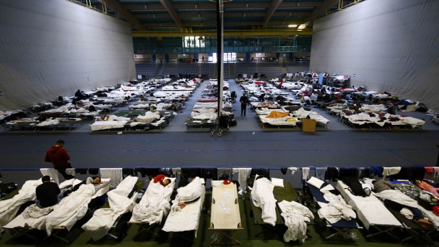 Migrants rest on beds at an improvised temporary shelter in a sports hall in Hanau
