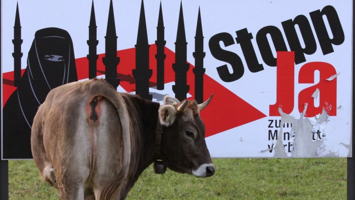 A cow stands in a meadow next to a display advertising the initiative against the construction of new minarets in