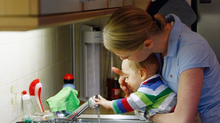 Leonard (ten-month-old) gets his mouth cleaned by mother Veronika Rixom in kitchen in Ismaning