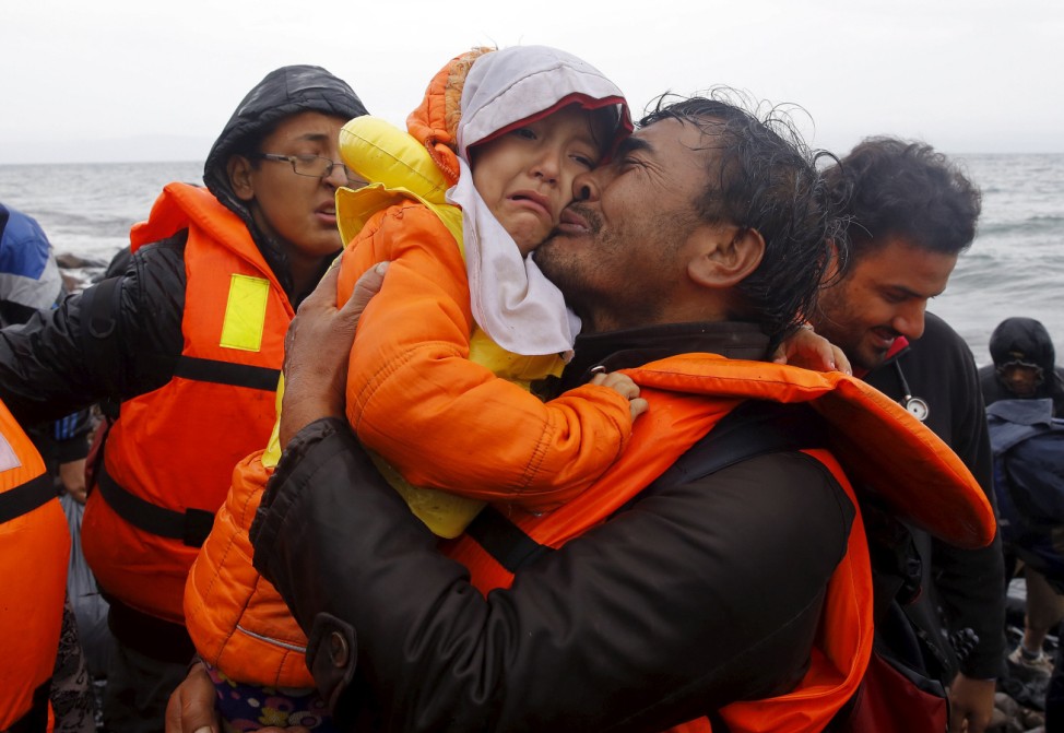 An Afghan migrant kisses his child moments after disembarking from a raft at a rocky beach during a rainstorm on the Greek island of Lesbos