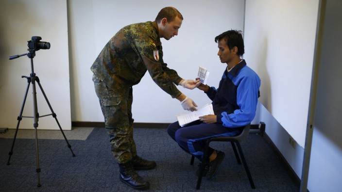 German soldier prepares migrant for identification photo at registration office of the Patrick-Henry Village refugee center a former U.S. military facility in Heidelberg