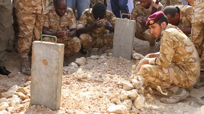 Qatari soldiers sit around the grave of their comrade, who was killed in Yemen, after his burial in Doha