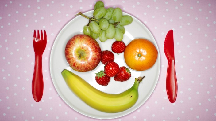 Plate with fruits building funny face and red plastic cutlery on pink cloth PUBLICATIONxINxGERxSUIxA