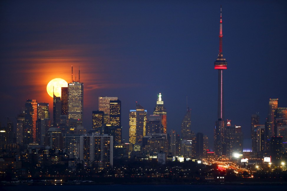 The moon rises behind the Canadian landmark CN Tower, and the skyline of Toronto