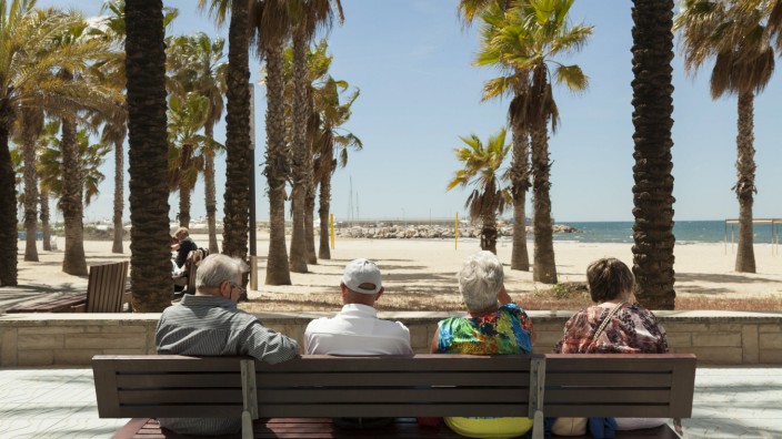 Rückansicht von Touristen die sich auf einer Bank ausruhen Ausblick auf Palmen und Strand Salou K