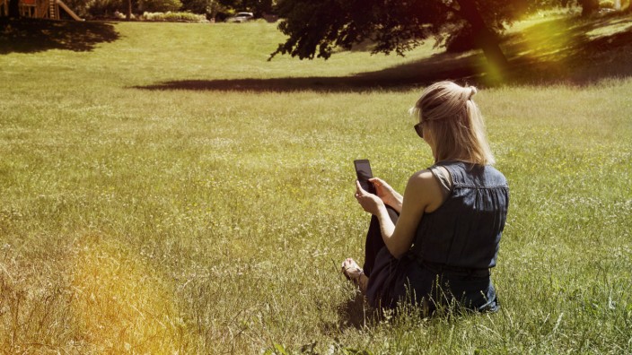 Woman sitting on a meadow of a park using smartphone model released Symbolfoto PUBLICATIONxINxGERxSU