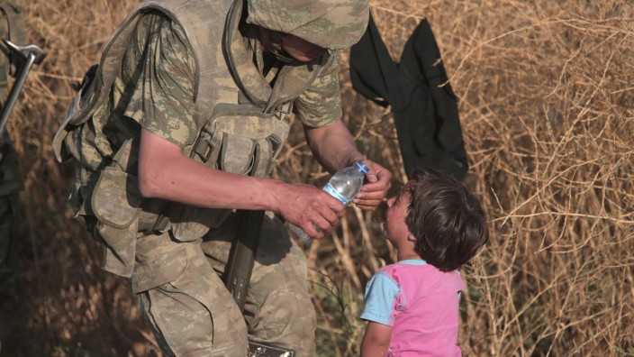 Ein türkischer Soldat bietet einem syrischem Flüchtlingskind Wasser an