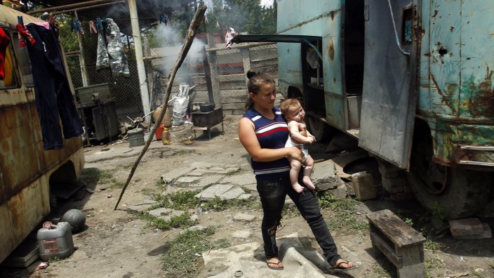 Chkadua, holding her nephew Misha, walks between abandoned buses which are used as shelter by her family in Tbilisi
