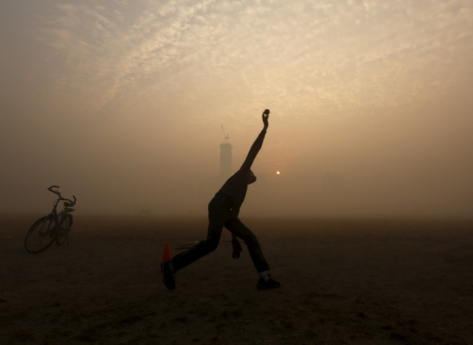 A boy bowls while playing cricket in a public park amidst heavy fog on a cold winter morning in Kolkata