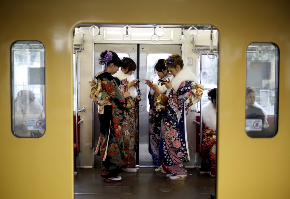 Japanese women wearing kimonos look at their mobile phones after their Coming of Age Day celebration ceremony at an amusement park in Tokyo