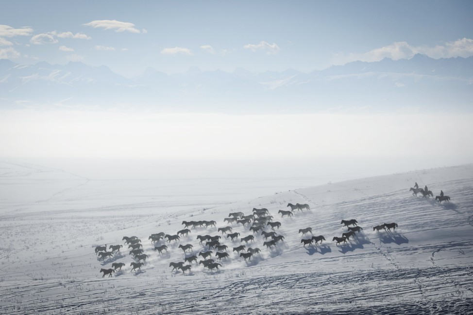 Herders ride horses on snow-covered field in Zhaosu County, Yili