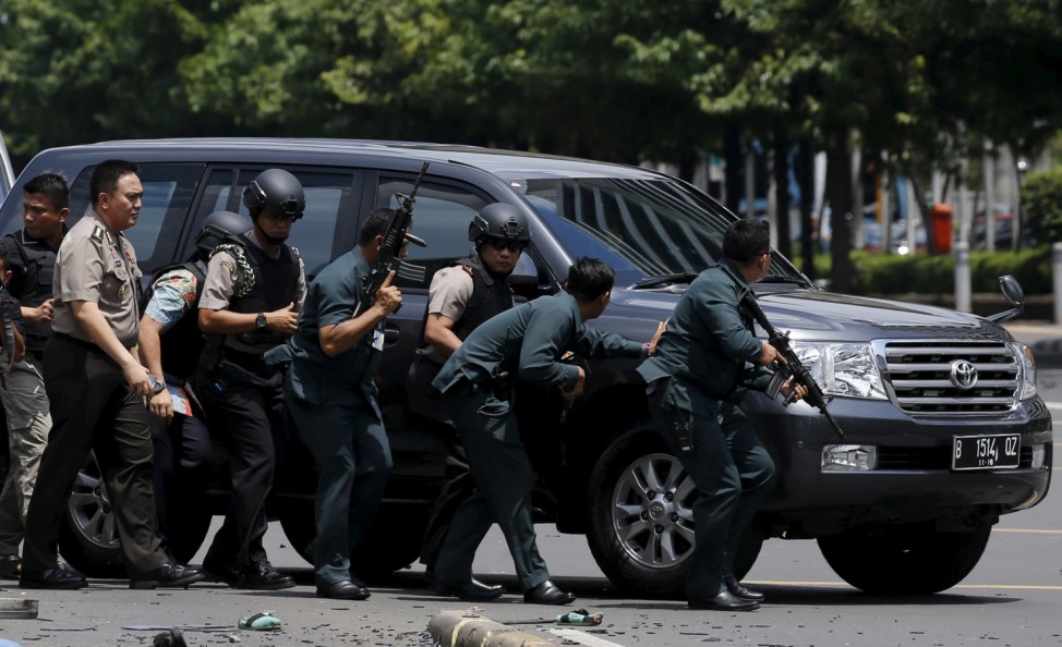 Indonesian police hold rifles while walking behind a car for protection in Jakarta