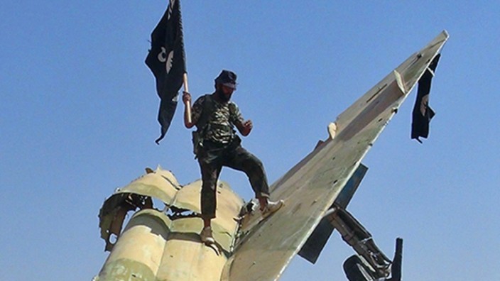 "Islamischer Staat": Schwarze Fahnen der Gewalt: IS-Terroristen posieren auf dem Wrack eines abgestürzten Kampfjets der syrischen Luftwaffe nahe Raqqa (Aufnahme von 2014).