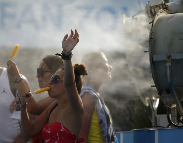Spectators cool off with popsicles in front of a misting fan at the Australian Open 2014 tennis tournament in Melbourne