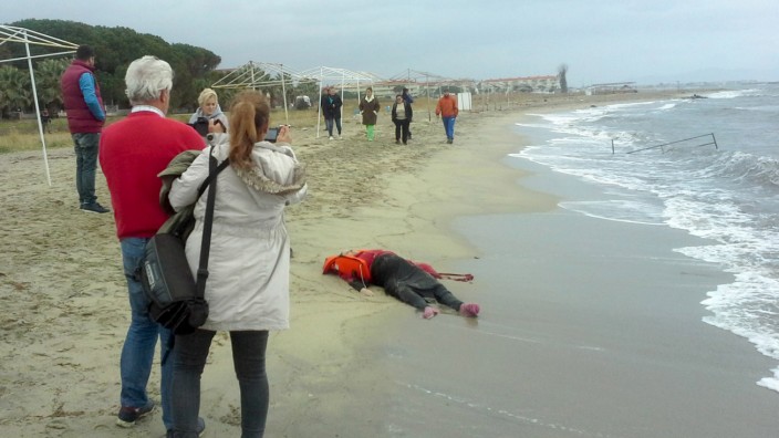 People take pictures as the body of a migrant lies on the shore in the Aegean coastal town of Ayvalik, Turkey
