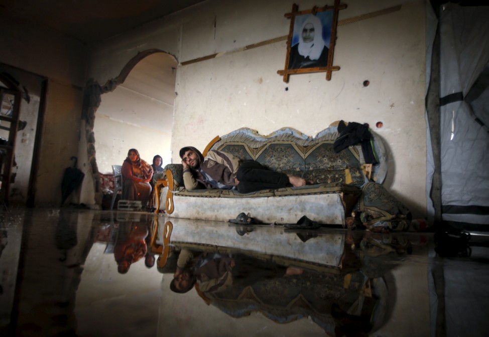 A Palestinian man lies on a couch in his flooded house that was damaged during the 2014 war, on a rainy day in Beit Hanoun in the northern Gaza Strip