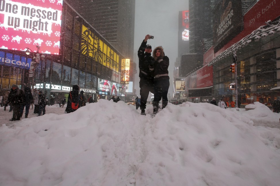 A couple poses for a photo on a snow pile during a snow storm in Times Square in the Manhattan borough of New York