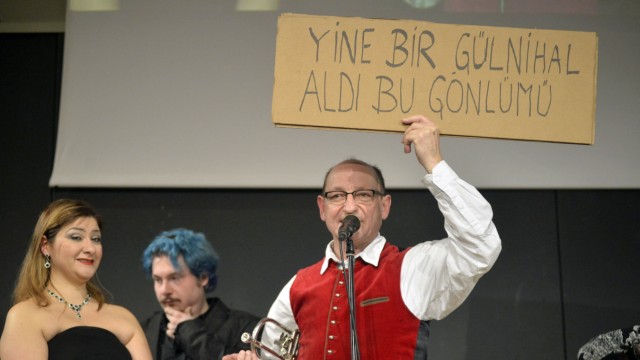 Neubiberg: Mit Liedstrophen in türkischer Sprache fordert Initiator Franz Josef Himpsl (rote Weste) das Publikum in Neubiberg zum mitsingen auf.