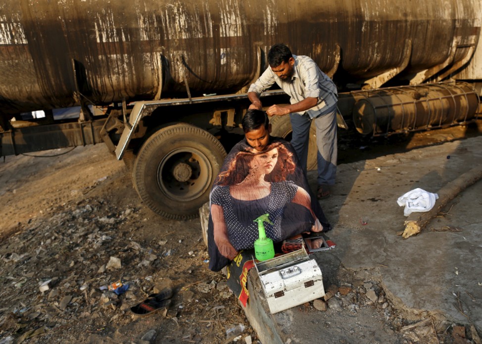 A truck driver gets a haircut from a roadside barber at an industrial area in Mumbai