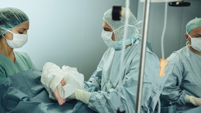 Surgeon handing over newborn to operating room nurse after c section PUBLICATIONxINxGERxSUIxAUTxHUNx