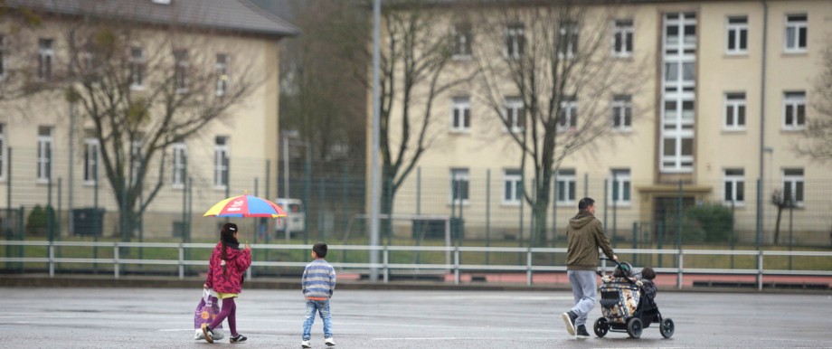 Migrant and his children walk in front of buildings in a refugee camp in Hameln