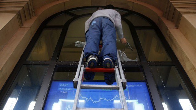 A window cleaner cleans a window in front of a television screen showing the German share price index DAX outside the stock exchange in Frankfurt