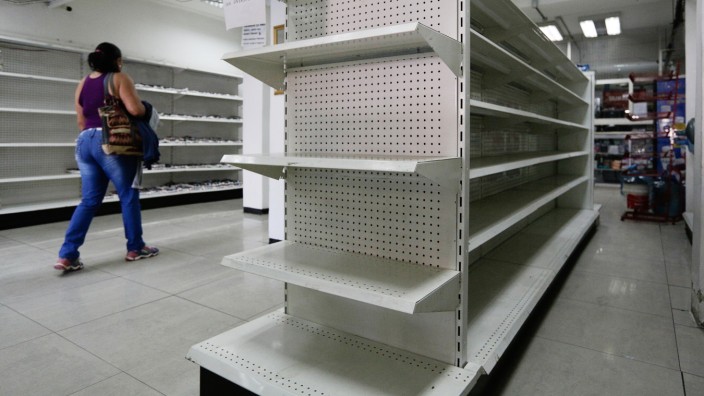 A woman walks past empty shelves at a drugstore in Caracas