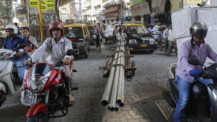 A porter transports metal pipes on a wooden handcart as people wait to cross a street in Mumbai