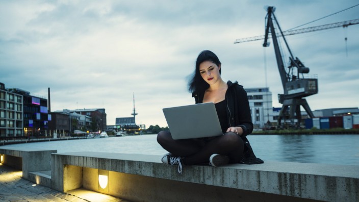 Germany, Muenster, young woman with laptop sitting in front of city harbour model released Symbolfot