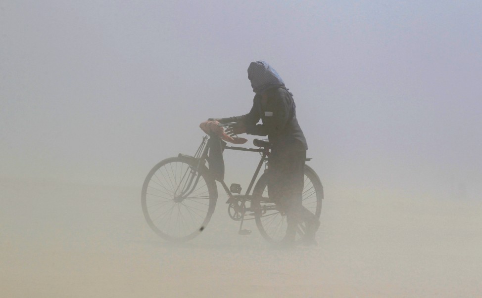 A man covers his face as he pushes a bicycle through a dust storm on the banks of the Ganga river in Allahabad