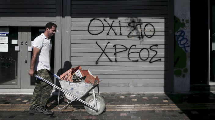 File photo shows graffiti on a closed Attica Bank branch reading, 'No to the debt' as a worker pushes a cart walks by in Athens
