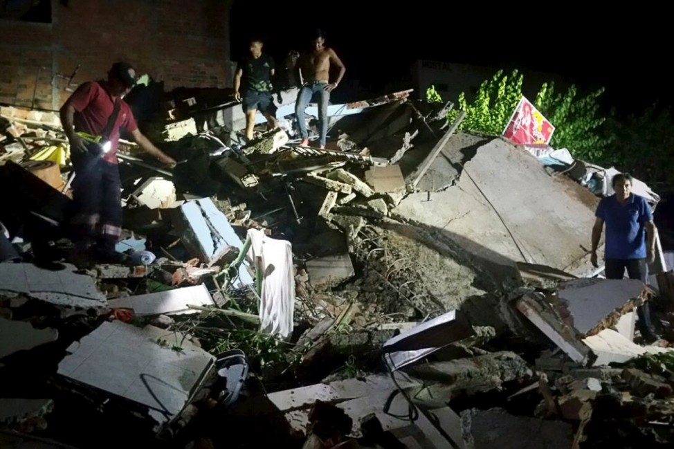 People stand next to the debris of a building after a 7.8 magnitude earthquake struck off the country's northwest Pacific coast causing 'considerable damage', in Manta