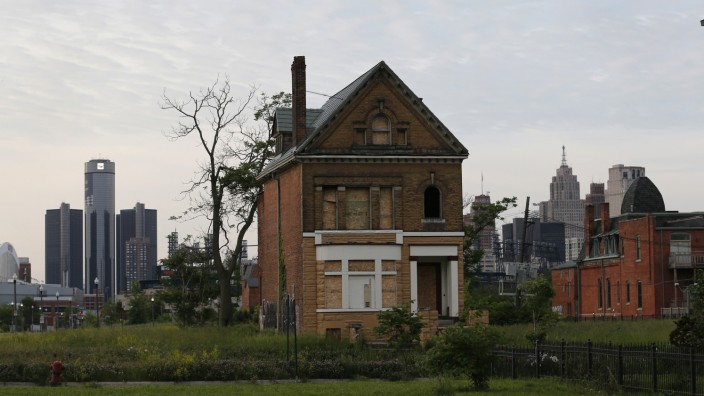 A boarded up vacant home is seen with General Motors World Headquarters and the Detroit skyline