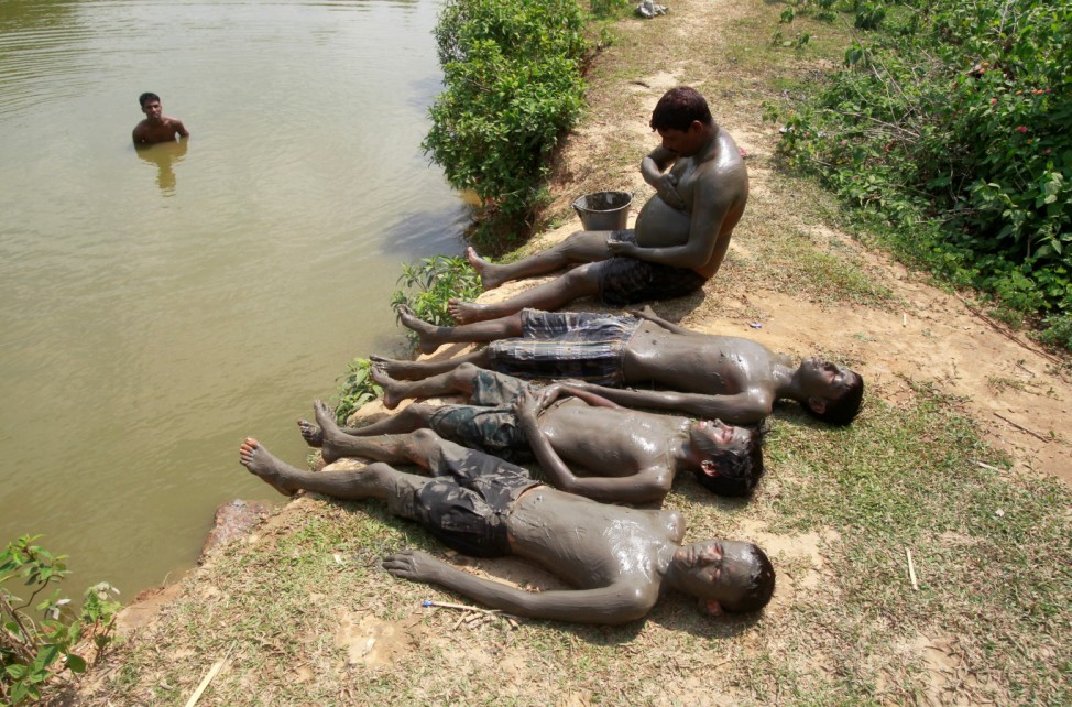 People relax after applying mud on their bodies to cool off on a hot summer day on the banks of the Kanchon Mala lake in the outskirt of Agartala