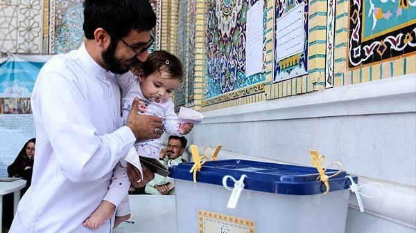 Iranian man holds a girl as he casts his vote during a second round of parliamentary elections, in Shiraz