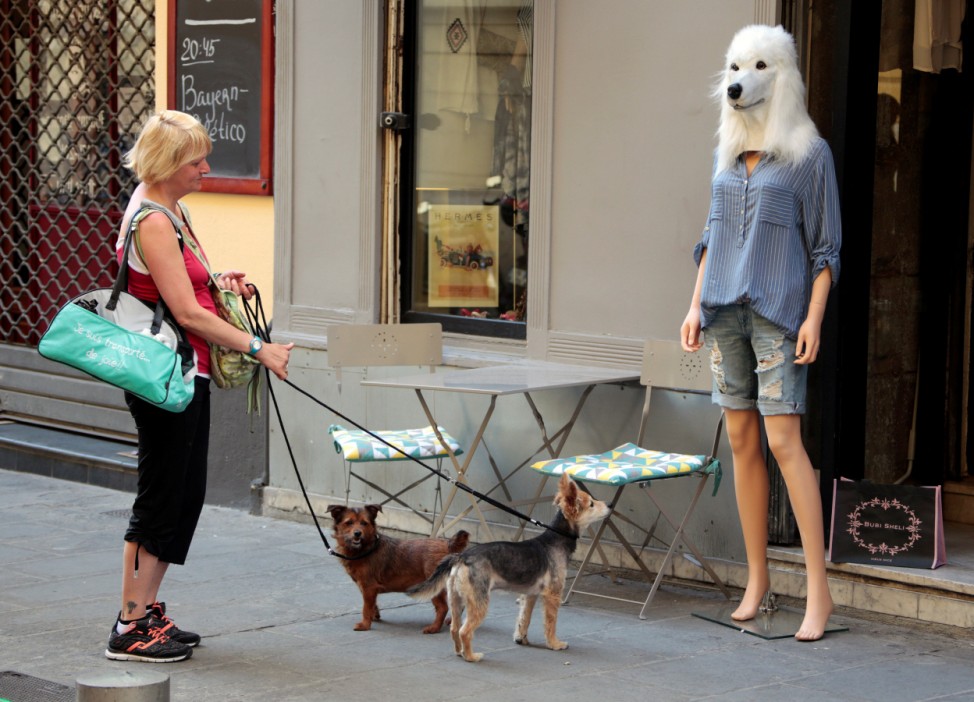 A woman and her dogs stop and look at a store mannequin wearing a dog's head mask outside a fashion shop in Nice