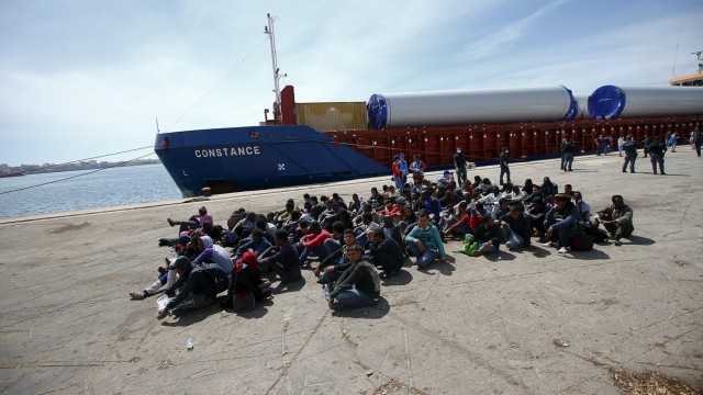 Migrants sit after disembarking from a merchant ship in the Sicilian harbour of Augusta