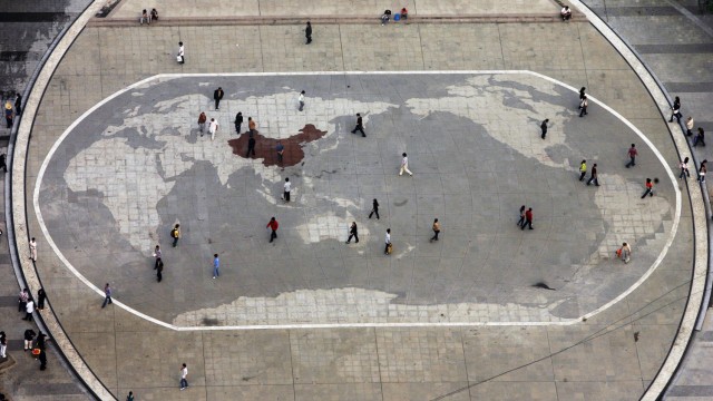 Kartografie: Ihre Sicht der Welt: Besucher in der Stadt Chongqing spazieren über eine Weltkarte, dunkel eingefärbt China.